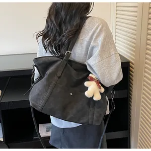 Detail of dark grey tote bag with adjustable strap and small white bear plush pendant