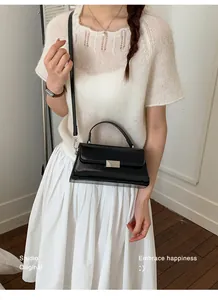 Detailed view of black shiny crossbody bag with silver buckle on elegant white outfit