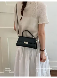 Detail of black rectangular leather handbag with silver lock and adjustable shoulder strap