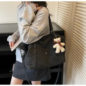 Detail of black textured tote bag featuring front pocket and cute plush bear charm