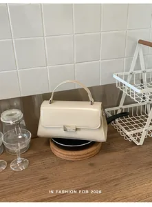 Detail of a creamy white leather handbag featuring a silver lock on a kitchen counter