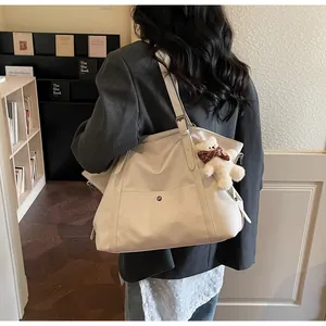 Close-up of off-white tote bag with teddy bear charm worn over the shoulder in a cozy setting