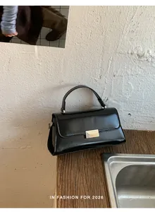 Chic black glossy leather crossbody bag with golden buckle on rustic wooden table
