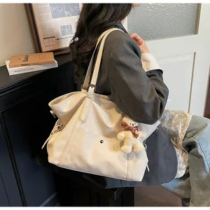 Detail of creamy tote bag featuring adjustable strap and cute plush bear charm detail