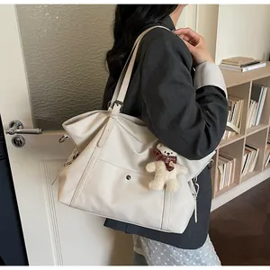 Detail of cream oversized tote bag with adjustable buckle strap and plush bear charm