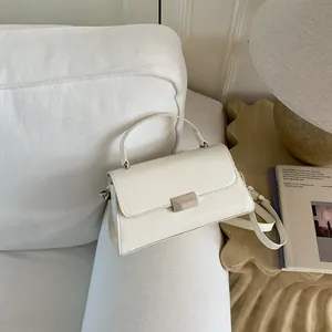 Elegant beige square handbag with top handle and crossbody strap on a white fabric sofa