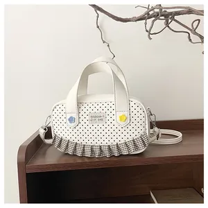Detail of white polka dot handbag featuring brown plaid ruffle trim and small floral patches