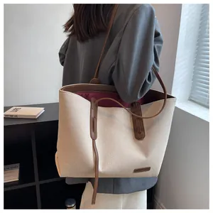 Detail of canvas tote bag with brown leather handles and brand plaque shown on model