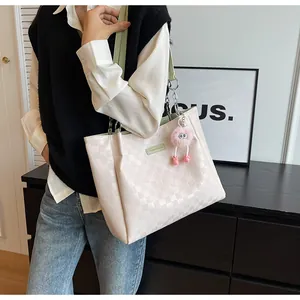 Detail of cream tote bag with checkered texture, green straps and pink plush charm