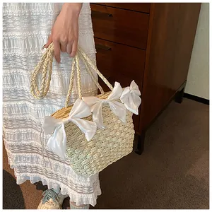 Détail du sac en paille beige avec trois nœuds en satin blanc et bandoulière tressée