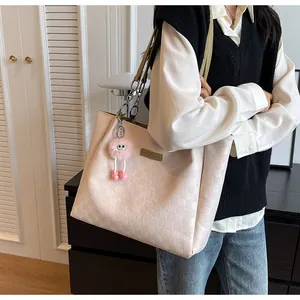 Detail of cream tote bag with embossed checkered texture, chain strap, and plush charm