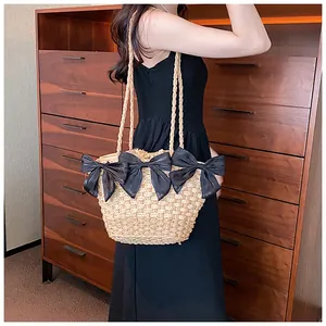 Détail du sac à bandoulière en paille avec trois nœuds en ruban noir et texture tissée fine