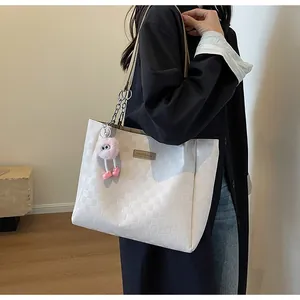 Macro detail of white checkered tote bag featuring an embossed leather patch and plush charm