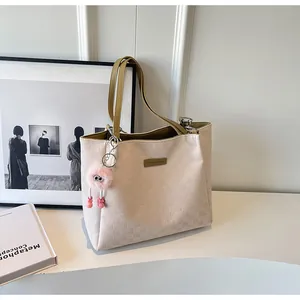 Close-up of embossed cream faux leather tote with olive straps and pink plush charm