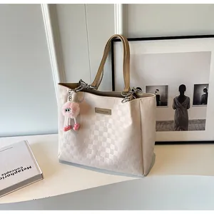 Detail of cream oversized tote bag with embossed lattice texture and pink plush charm