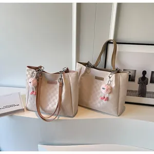Macro detail of checkered embossed tote bags with pink plush charms in a white minimalist setting