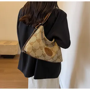 Detail view of canvas monogram tote bag with chain strap on model in black blazer