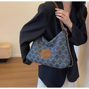 Detail of blue denim tote bag with monogram pattern and leather patch featuring M embossing