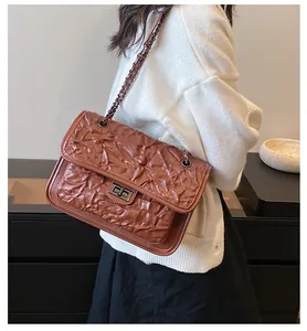 Sac bandoulière marron matelassé avec chaîne en métal porté par un mannequin