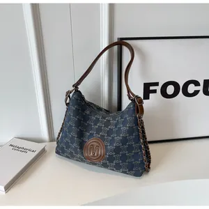 Detail of vintage canvas hobo bag with denim pattern and brown leather letter M patch