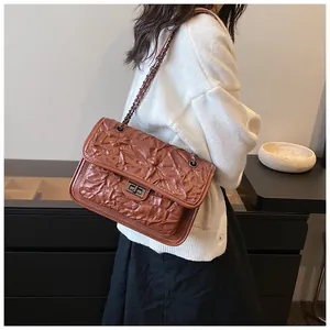 Détail d'un sac bandoulière marron matelassé avec chaîne en métal et fermoir rotatif