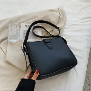 Schwarze Leder-Eimertasche mit Goldbeschlägen und verstellbarem Gurt auf neutralen Laken