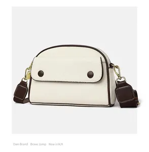 Detail of creamy white pebble leather crossbody bag with wide brown fabric strap