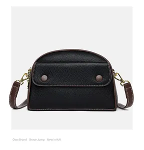 Close-up of black lychee grain texture with brown leather trim and gold metal hardware