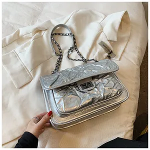 Détail du sac argenté plissé avec fermoir rotatif et bandoulière chaîne sur blazer blanc