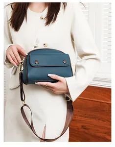 Close-up of teal leather crossbody bag with brown trim and adjustable wide nylon strap