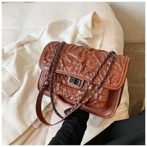 Détail d'un sac bandoulière en cuir matelassé marron avec chaîne en métal et fermoir rotatif
