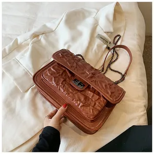 Détail de la texture matelassée marron avec fermoir rotatif et bandoulière en chaîne