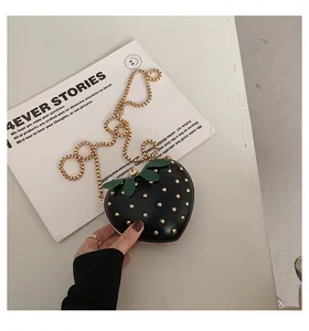 Macro detail of strawberry-shaped mini bag in black leather with golden rivets and leaf