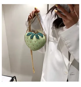 Detail showing a light green strawberry bag with gold studs and metal chain strap