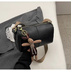 Detail of black cylinder crossbody bag with woven wide strap and plush bunny charm