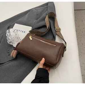 Detail of dark brown leather Boston bag with gold hardware and wide woven strap