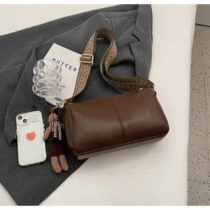 Brown leather crossbody pillow bag with patterned wide strap and rabbit charm on a suit