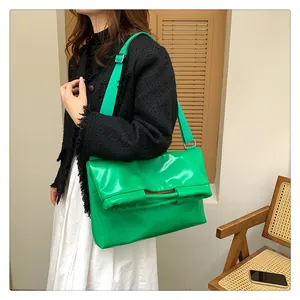 Detailansicht der smaragdgrünen glänzenden Tasche mit breitem Gurt an einem Model