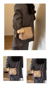 Detail of beige pleated crossbody bucket bag with cute plush bear charm and knot accent