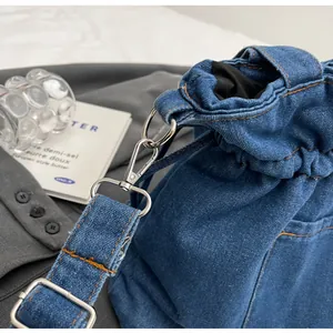Detail of blue denim bucket bag with orange contrast stitching and silver metal hardware