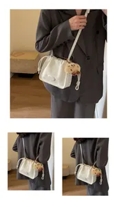 Detail of white pleated crossbody bucket bag with branding and plush animal charm