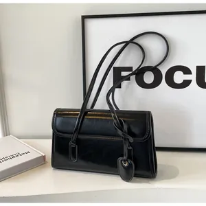 Close-up of black glossy leather underarm bag with unique heart-shaped charm and strap