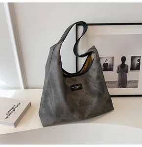 Detailed view of large grey tote bag with leather straps on a white pedestal