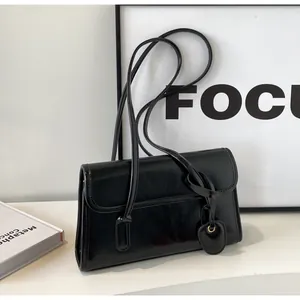 Detail of a black glossy leather shoulder bag with sleek straps on a minimalist display