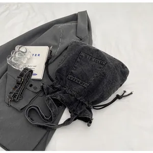 Detail of dark gray washed denim bucket bag featuring drawstring closure and front pocket