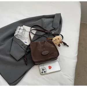 Detail of retro pleated dark brown crossbody bag with bear charm and adjustable strap