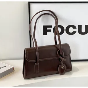 Detail of dark brown glossy underarm bag with decorative heart tag and mirror finish