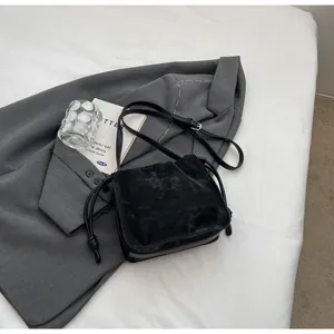 Close-up of black pleated crossbody bucket bag with side knot detail on grey blazer background