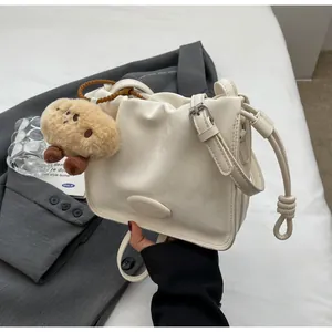 Close-up of cream crossbody bucket bag with pleated details and plush biscuit charm