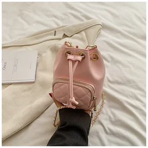 Sac seau rose matelassé avec bandoulière chaîne dorée posé sur un drap blanc